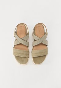 Grønne semskede sandaler med kryssede elastiske remmer, polstret såle og en bred stropp ved tåen. Flat såle for komfort.