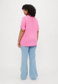 Lys rosa kortermet topp med rullekant, kombinert med lyseblå utvidede jeans. Skjorten har en teksturert overflate og en avslappet passform.