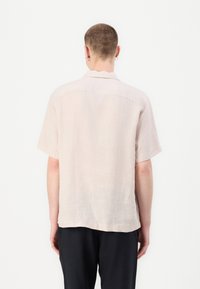 Camisa de manga curta rosa claro, feita de linho, com um corte descontraído, apresentando um colarinho clássico e bainha reta, vista de trás.