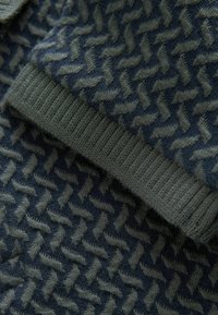 Maglione lavorato a maglia con un motivo a zigzag in blu scuro e verde oliva. La texture è morbida, con polsini e orlo a coste per una vestibilità aderente.