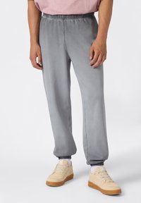Grijze, zachte stoffen sweatpants met een elastische tailleband en geribde manchetten, gecombineerd met beige sneakers. Eenvoudig ontwerp zonder zichtbare patronen.