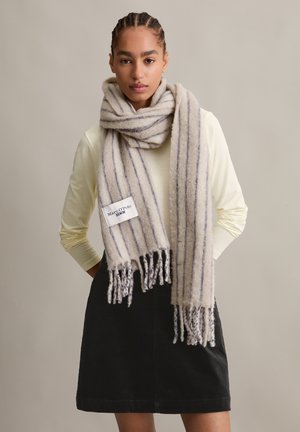 Beige and gray striped scarf made of soft wool, featuring fringe ends and a label displaying "Marc O'Polo Denim." Worn over a light top.