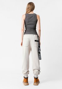 Top gris sin mangas con tirantes estrechos; pantalones de chándal sueltos de color beige claro con bolsillos; botas marrones hasta el tobillo; etiqueta colgando de los pantalones.