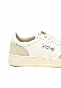 Zapatilla blanca con acentos de ante, que presenta una superficie texturizada, puntera redonda y logo en el lateral. Suela de color crema con suela estriada.