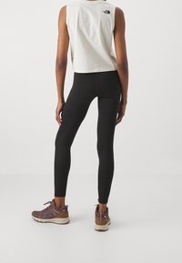 Leggings neri con un design aderente, abbinati a un top corto bianco con un logo nero e scarpe da trekking marroni.