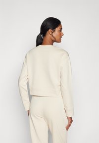 Felpa corta color crema con scollo rotondo e polsini a coste, realizzata in un materiale morbido. Presenta una texture liscia e una vestibilità comoda.