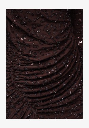 Brązowa marszczona tkanina ozdobiona małymi czarnymi cekinami i kwiatowymi zdobieniami, tworząca teksturowany, warstwowy wygląd.