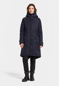 Marinblå vattentät jacka med huva, hel dragkedja, sidfickor, justerbara ärmslut och en lätt utsvängd fåll för rörelsefrihet.