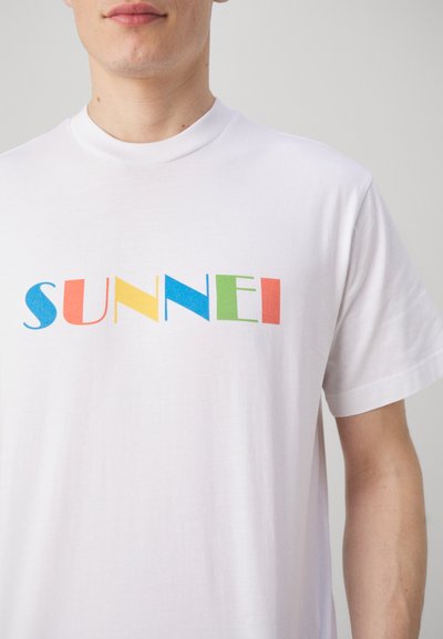 White cotton t-shirt featuring the word "SUNNEI" in bold, colorful letters: blue, yellow, red, green, and orange. Short sleeves, crew neckline.