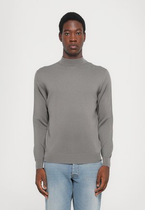 Gray knitted sweater with a high neck, long sleeves, and a fitted design, paired with light blue jeans. Soft texture and minimal detailing.
