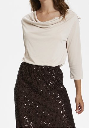 Femme portant un haut crème à col bénitier et manches trois-quarts avec une jupe noire à sequins.