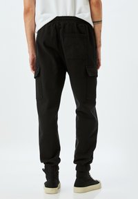 Zwarte cargobroek met een relaxte pasvorm, elastische tailleband en taps toelopende cuffs. Inclusief patchzakken aan de zijkanten en een achterzak.