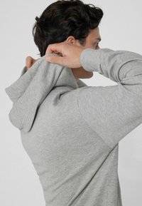 Hellgrau Hoodie aus weichem Stoff. Verfügt über eine Kapuze mit Kordelzug, lange Ärmel und gerippte Bündchen. Sanfte Textur und lässige Passform.