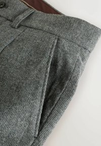 Gray tailored trousers made of textured fabric featuring a subtle houndstooth pattern, with a traditional waistband and angled pockets.