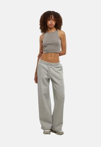 Crop top grigio a coste abbinato a pantaloni della tuta grigi larghi, con cintura elastica e cordoncino. Il modello indossa sneakers chiare.