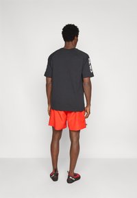 Μαύρο κοντομάνικο μπλουζάκι συνδυασμένο με φωτεινά κόκκινα σορτς. Το μπλουζάκι έχει απλό σχέδιο· τα σορτς έχουν λεία υφή, ιδανικά για καθημερινή χρήση.