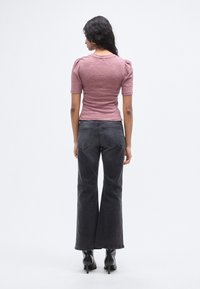 Εφαρμοστό, ριμπ ροζ πουλόβερ με κοντά φουσκωτά μανίκια; Συνδυασμένο με ψηλόμεσα, φαρδιά μαύρα τζιν παντελόνια; Το μοντέλο φοράει μαύρα μπότες με τακούνι.