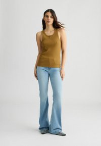 Débardeur côtelé beige associé à un jean évasé bleu clair. Tissu texturé, coupe ajustée, et chaussures à talons pointus noires et blanches à carreaux.