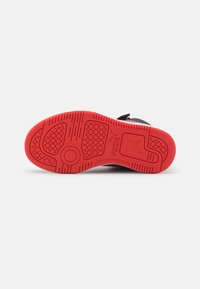 Zwarte sneakerzool met rode rubberen buitenzool, voorzien van een honingraatpatroon, groeven en een cirkelvormig accent. Duurzaam materiaal voor grip.