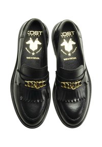 Mocassins en cuir noir avec un accent de chaîne dorée, des pampilles et une texture lisse. Fabriqués au Portugal, avec un bout rond et une semelle plate.