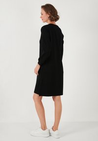 Black dress with long sleeves, mid-thigh length, soft texture, relaxed fit, and side slits, paired with white sneakers.
