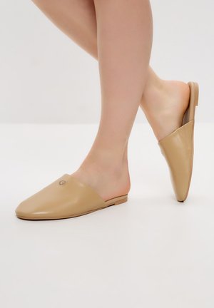 Scarpe slip-on beige con una texture in pelle liscia, punta affusolata e un discreto dettaglio del logo sulla parte superiore. Suola piatta senza supporto posteriore.