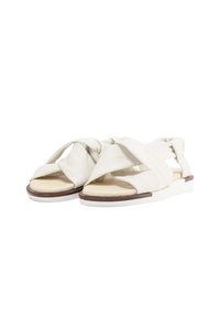 Lys beige sandaler med brede tværsnitsremme, glat lædertekstur og en flad hvid sål med brun detalje. Åben tå-design.