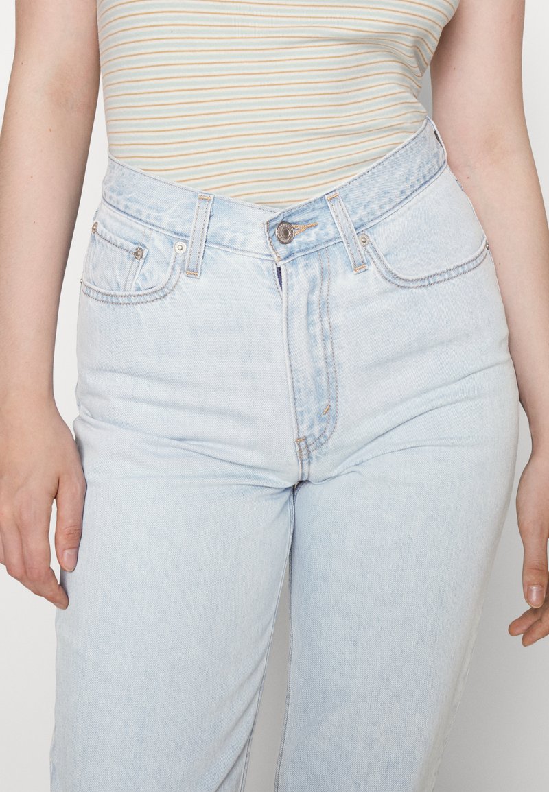 Hellblaue, hoch geschnittene Jeans aus Denim mit einem verwaschenen Finish, ausgestattet mit einem klassischen Fünf-Taschen-Design und kupferfarbenen Nieten.