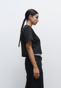 Maglietta nera cropped a maniche corte, realizzata in tessuto di cotone; abbinata a jeans neri a vita alta con dettagli in metallo argento.