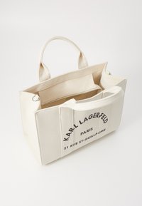Sac fourre-tout en toile beige avec des poignées courtes, doté d'une poche zippée à l'intérieur et d'un texte imprimé : "KARL LAGERFELD PARIS 21 RUE ST-GUILLAUME."