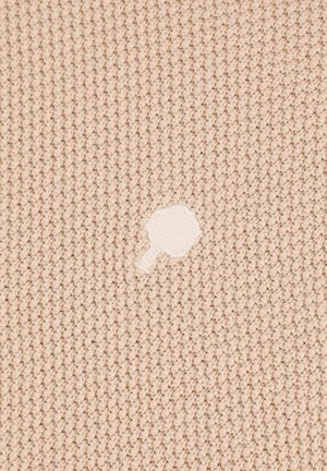 Beige knitted fabric with a textured pattern featuring a small white irregular patch or hole in the center.