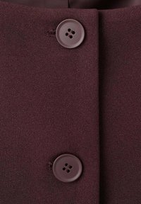 Material burgund cu o textură netedă, având două nasturi rotunzi maro și o cusătură. Materialul prezintă un luciu subtil.