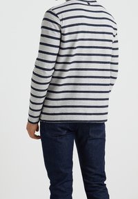 Chemise grise à manches longues avec des rayures horizontales bleu marine, dotée d'un col rond et d'un ourlet droit, associée à un jean en denim foncé.