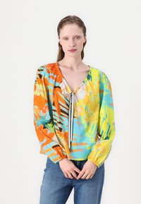 Blouse multicolore arborant un motif abstrait vibrant d'orange, bleu et jaune, avec un décolleté en V et des poignets élastiqués.