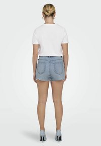 Shorts in denim con orlo sfilacciato, lavaggio azzurro chiaro, design a cinque tasche, abbinati a una maglietta bianca e tacchi alti azzurri.