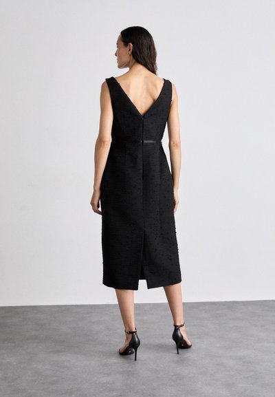 Svart midiklänning med ett strukturerat mönster, V-formad rygg och definierad midja. Har en dragkedja i ryggen och en slits i fållen för bättre rörelsefrihet.