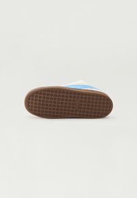 Brun gummisåle til sneakers med en teksturert mønster med geometriske former; lyseblå og hvite detaljer langs skoens kanter.
