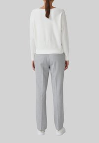 Pull en tricot blanc avec un ourlet côtelé, associé à un pantalon taille légère gris clair. Le modèle porte des baskets blanches. Design simple et épuré.