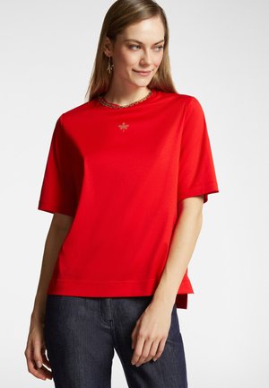 Camiseta roja de manga corta con un corte relajado, que presenta un escote decorativo y un pequeño detalle de libélula bordada en el pecho.