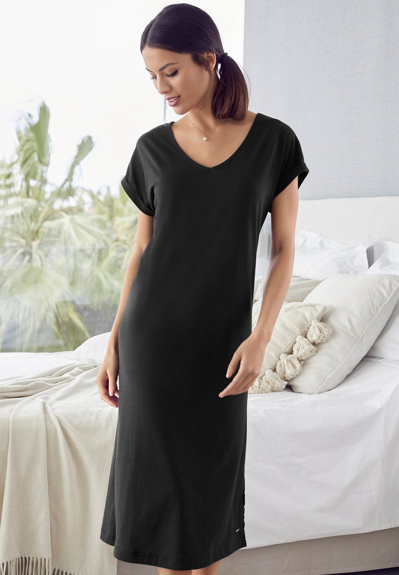 Zwarte katoenen jurk met een V-hals, korte opgerolde mouwen en een lose pasvorm, tot halverwege de kuit. Heeft een zachte textuur en zijsplitsen.