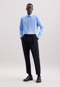 Camicia a righe blu chiaro con bottoni abbinata a pantaloni tailleur neri scuri e scarpe eleganti nere, caratterizzata da un design elegante e aderente.