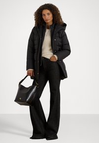 Μαύρο μπουφάν με κουκούλα, υφασμάτινη κρέμα πουλόβερ, σκούρες καμπάνα τζιν και μαύρη τσάντα με κροκοδείλινη υφή και χρυσές λεπτομέρειες.