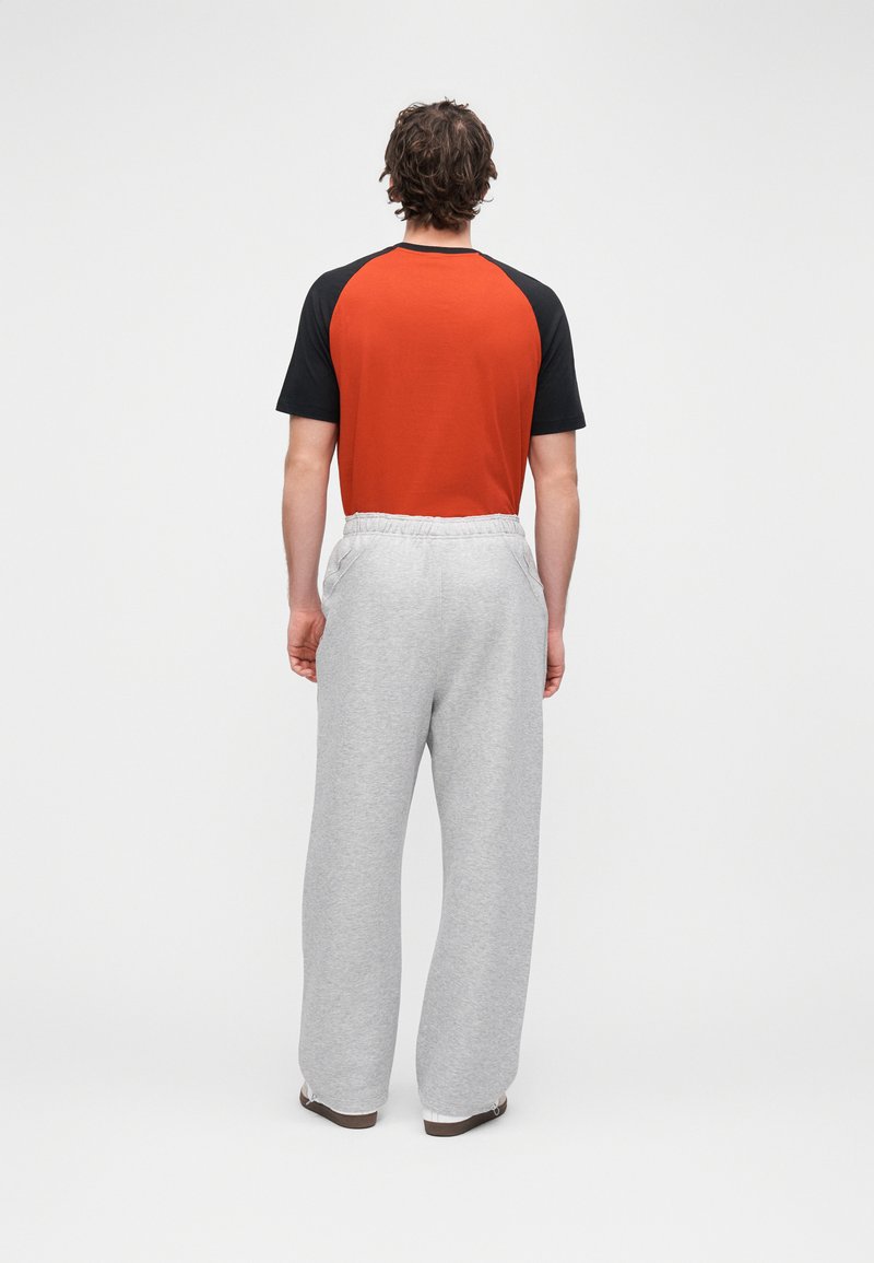 Tenue pour homme comprenant un T-shirt à manches courtes rouge et noir et un pantalon de survêtement gris. Le pantalon possède une ceinture élastique et une coupe décontractée.