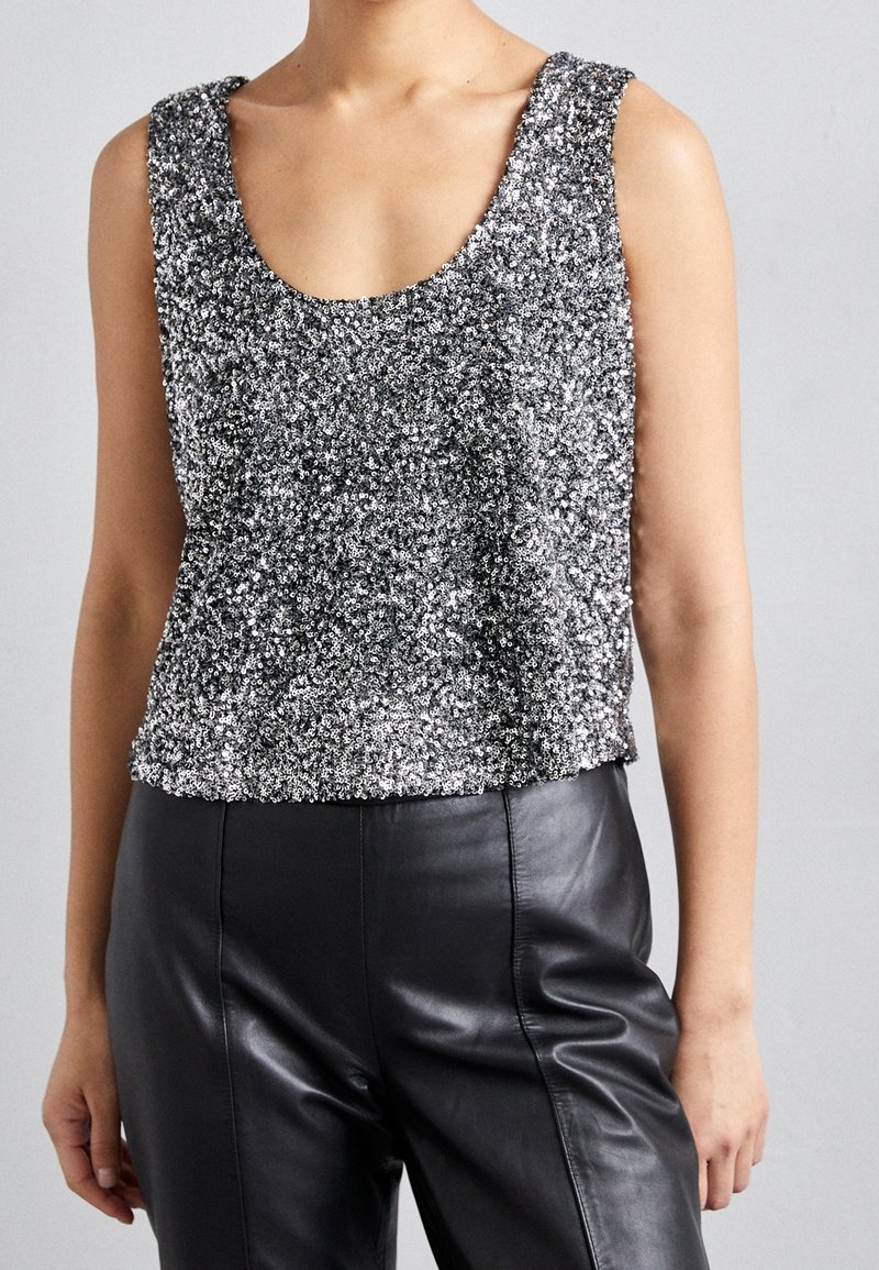 Débardeur argenté orné de sequins, à encolure dégagée, sans manches, et coupe ample, associé à un pantalon en cuir noir.