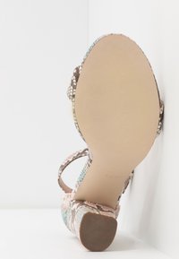 Sandale à talons hauts avec un design imprimé serpent en beige, rose et bleu. Dispose d'une semelle texturée et de plusieurs brides pour un bon maintien.