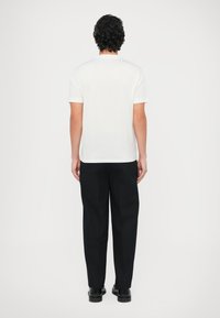 Biały T-shirt z krótkim rękawem wykonany z bawełny, zestawiony z czarnymi spodniami. Materiał wydaje się gładki, o regularnym kroju, bez widocznych logo ani wzorów.