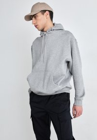 Grå hettegenser med snor i halsen, lommer foran og ribbede mansjetter, kombinert med sorte cargo-bukser og en beige caps. Enkelt, uformelt design.