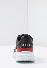 Baskets noires avec une tige texturée, accent rouge et une semelle bicolore mouchetée blanche. Présente un logo en relief au niveau du talon.