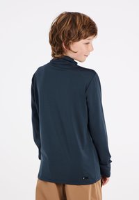 Donkerblauw langmouwtop met een hoge kraag, gladde structuur en logo aan de zoom. Heeft een ontspannen pasvorm en lichte stof.