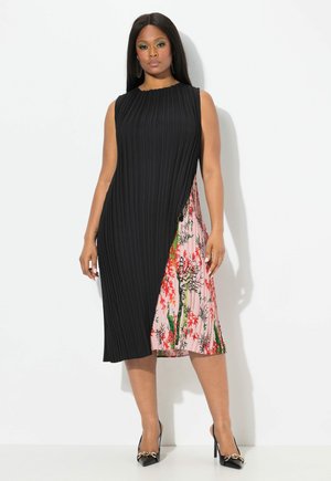 Schwarzes plissiertes Kleid mit einem seitlichen Einsatz im floralem Muster in Pink, mit fließendem Design und ärmellosem Schnitt. Schwarze High Heels.